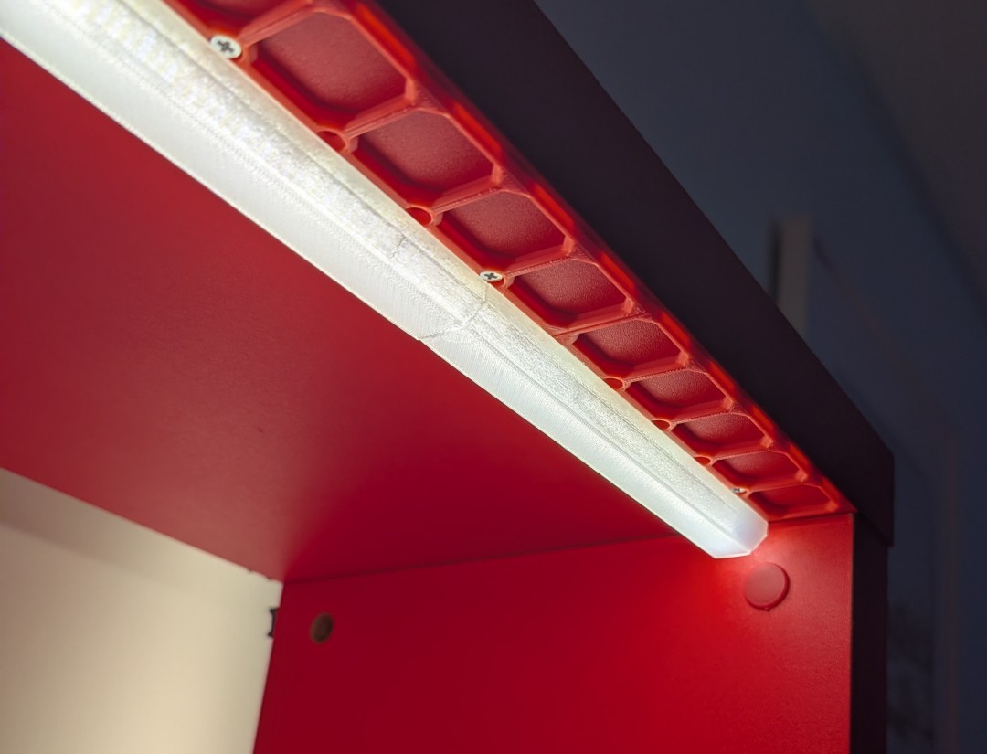 LED diffuser over an illumenated LED strip on the underside of a red shelf.  It is supported by a red plastic grid.  The light fills the bar created by the diffuser.